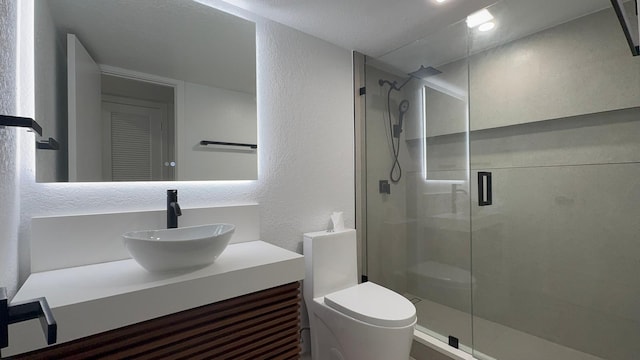 full bath with a textured wall, vanity, toilet, and a stall shower