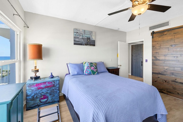 bedroom with a ceiling fan, visible vents, a barn door, and light wood-style floors
