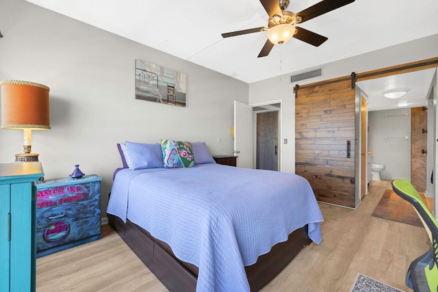 bedroom featuring wood finished floors, visible vents, ensuite bath, and a barn door