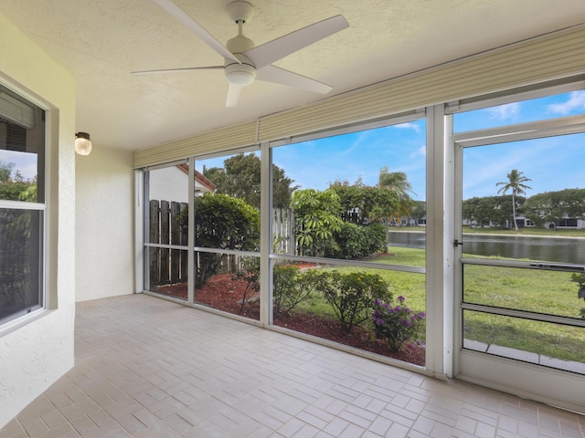 unfurnished sunroom featuring brick floor, a water view, and a ceiling fan