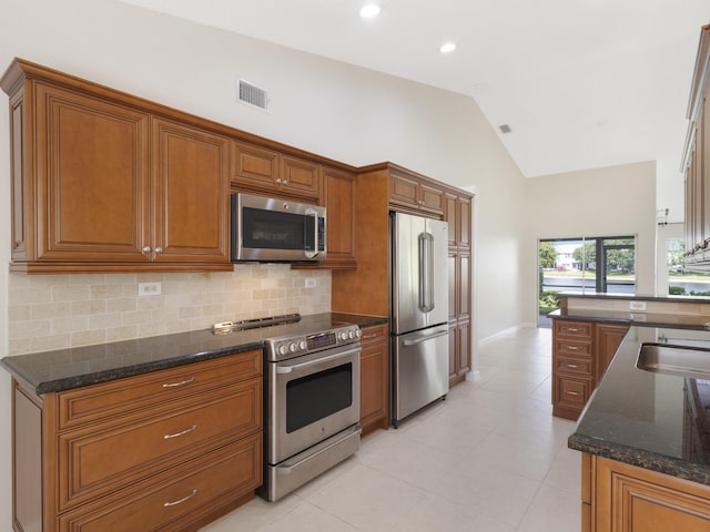 kitchen with backsplash, visible vents, dark stone counters, brown cabinetry, and appliances with stainless steel finishes