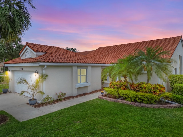 mediterranean / spanish house featuring a tile roof, concrete driveway, an attached garage, a yard, and stucco siding