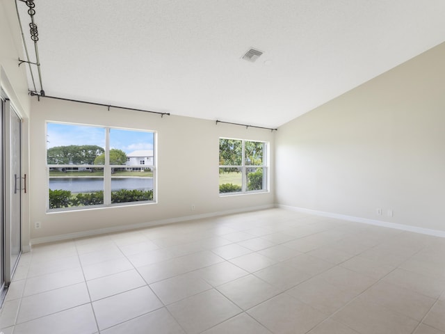 spare room featuring a water view, light tile patterned flooring, vaulted ceiling, baseboards, and visible vents