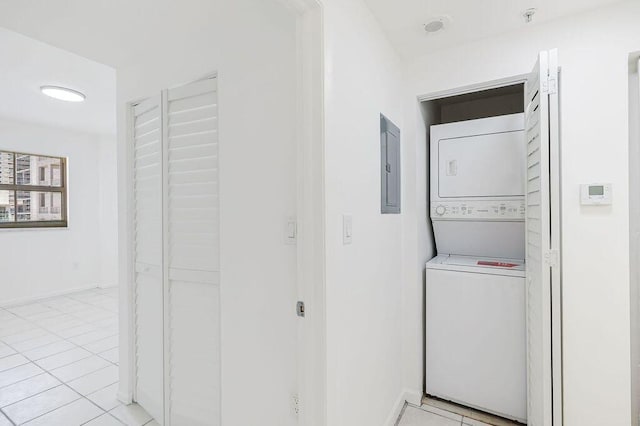 laundry area featuring electric panel, light tile patterned floors, baseboards, stacked washer and clothes dryer, and laundry area