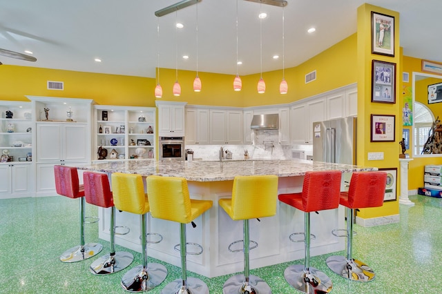 kitchen featuring visible vents, light stone countertops, wall chimney exhaust hood, appliances with stainless steel finishes, and white cabinetry