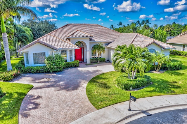 mediterranean / spanish-style house with a tiled roof, driveway, a front lawn, and stucco siding
