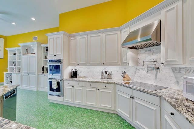 kitchen with stainless steel double oven, black electric cooktop, backsplash, wall chimney exhaust hood, and white cabinetry