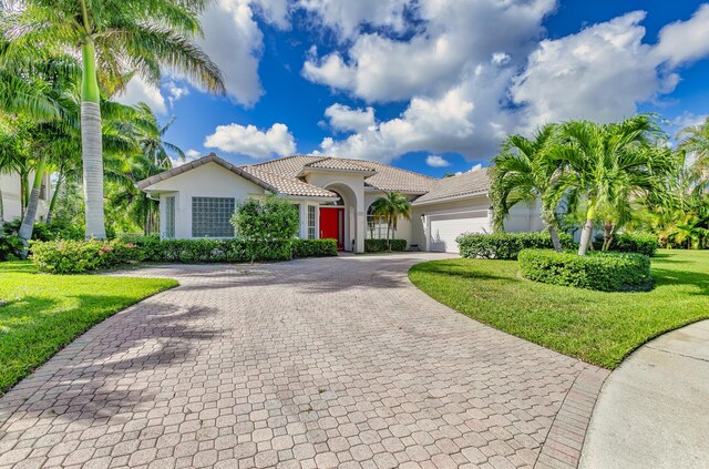 view of front facade featuring stucco siding, a tile roof, decorative driveway, a front yard, and a garage