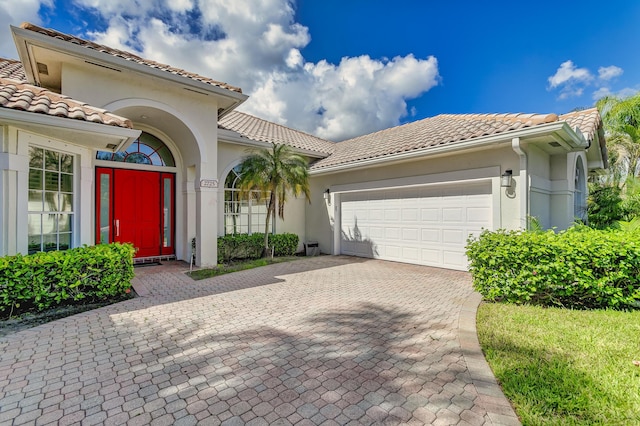 mediterranean / spanish house with a garage, a tile roof, stucco siding, and decorative driveway