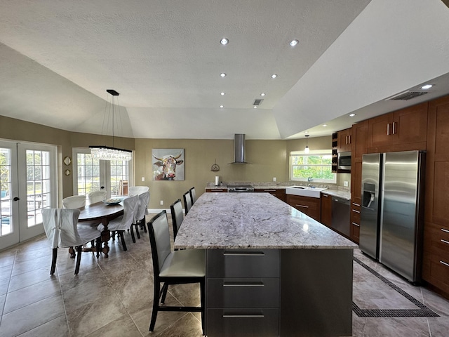 kitchen with appliances with stainless steel finishes, wall chimney exhaust hood, vaulted ceiling, a kitchen island, and visible vents