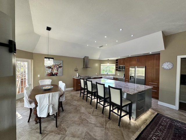 kitchen with vaulted ceiling, appliances with stainless steel finishes, wall chimney exhaust hood, and a center island