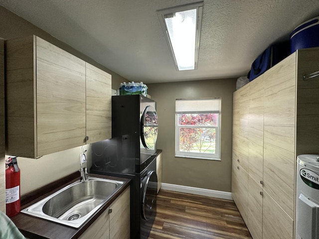 clothes washing area with dark wood-style flooring, cabinet space, stacked washing maching and dryer, baseboards, and a sink