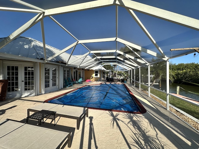 view of pool featuring french doors, a covered pool, a patio area, a water view, and glass enclosure