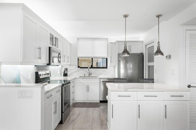kitchen featuring stainless steel appliances, a sink, white cabinetry, pendant lighting, and a kitchen island