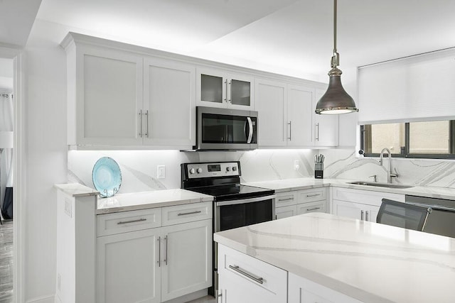 kitchen featuring light stone countertops, a sink, appliances with stainless steel finishes, and hanging light fixtures