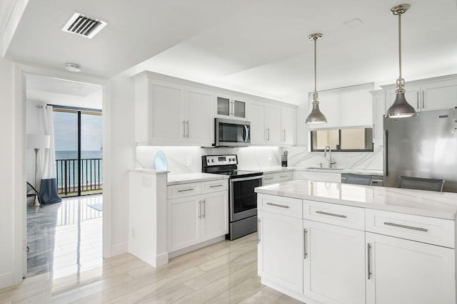 kitchen with stainless steel appliances, visible vents, a sink, decorative light fixtures, and white cabinetry