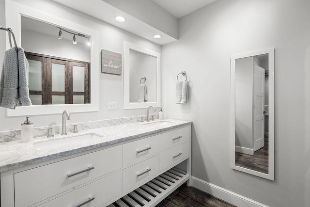 bathroom with baseboards, wood finished floors, a sink, and double vanity