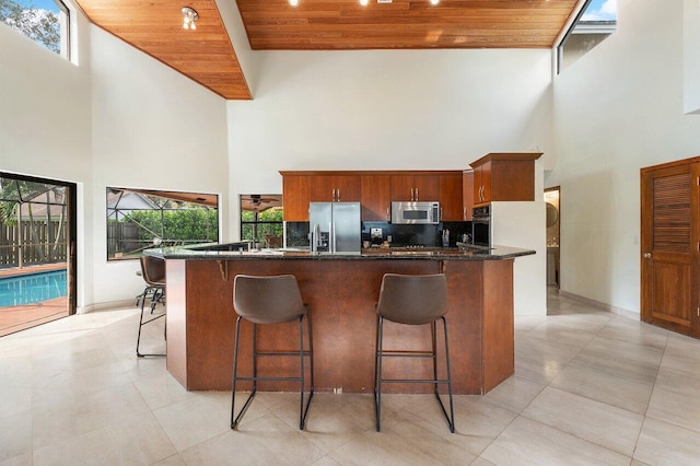 kitchen with a kitchen breakfast bar, stainless steel appliances, decorative backsplash, a towering ceiling, and wood ceiling