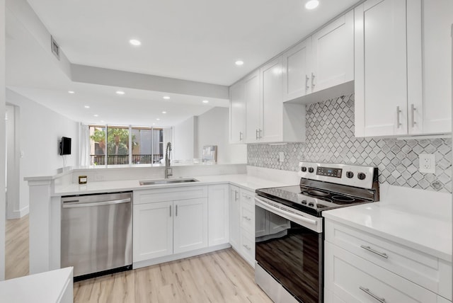 kitchen with white cabinets, a sink, light wood-style floors, decorative backsplash, and appliances with stainless steel finishes