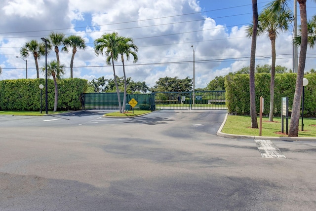 view of street with a gate, a gated entry, curbs, and street lights
