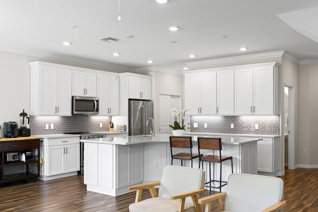 kitchen featuring stainless steel appliances, a center island with sink, decorative backsplash, light countertops, and crown molding