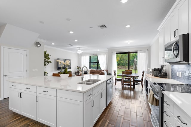 kitchen with appliances with stainless steel finishes, a sink, ornamental molding, dark wood finished floors, and a kitchen island with sink