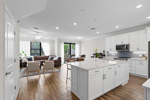 kitchen with stainless steel microwave, crown molding, a sink, light countertops, and white cabinets