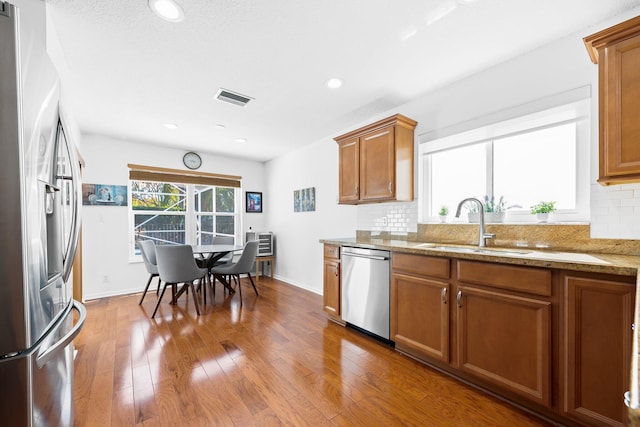 kitchen featuring stainless steel appliances, a sink, visible vents, decorative backsplash, and brown cabinets