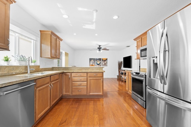 kitchen featuring recessed lighting, stainless steel appliances, a sink, wood-type flooring, and a peninsula