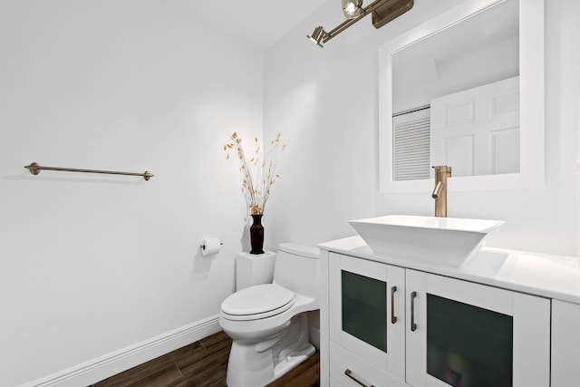 half bathroom featuring baseboards, wood finished floors, vanity, and toilet
