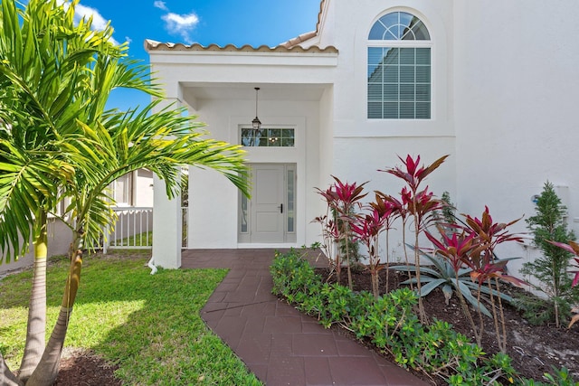 property entrance with a tile roof, a lawn, and stucco siding