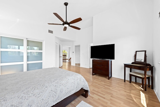 bedroom with light wood-type flooring, a ceiling fan, a towering ceiling, and visible vents
