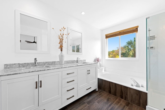 full bathroom with a garden tub, wood finished floors, a sink, and double vanity
