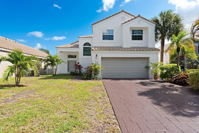 mediterranean / spanish house with a tile roof, decorative driveway, a garage, a front yard, and stucco siding