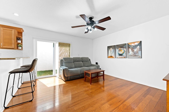 living room featuring light wood finished floors, baseboards, and ceiling fan