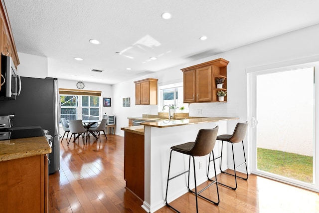 kitchen featuring stainless steel microwave, light wood-style flooring, a peninsula, brown cabinetry, and a breakfast bar area