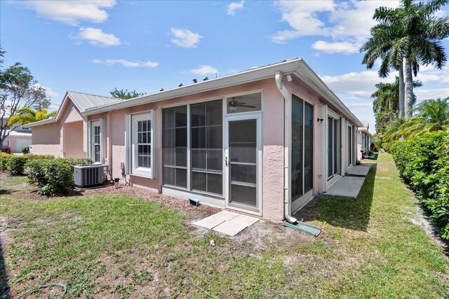 rear view of house featuring central AC, a lawn, metal roof, stucco siding, and a sunroom