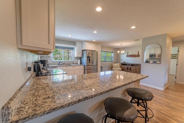 2675 SW 24th Ave, Okeechobee, FL 34974 - kitchen featuring appliances with stainless steel finishes, a peninsula, a breakfast bar, light stone countertops, and light wood-type flooring