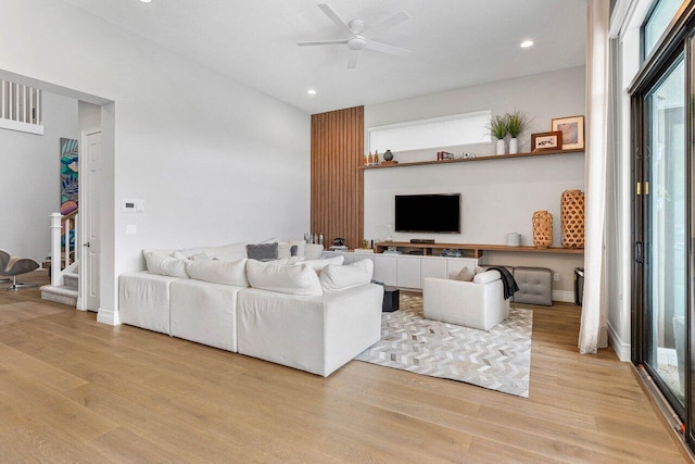 living room featuring a ceiling fan, light wood finished floors, a healthy amount of sunlight, and stairway