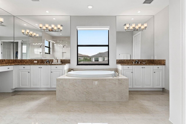 full bath featuring an inviting chandelier, a sink, two vanities, a garden tub, and a stall shower