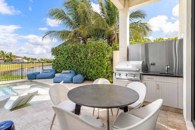 view of patio / terrace featuring fence, an outdoor kitchen, a water view, a sink, and a grill
