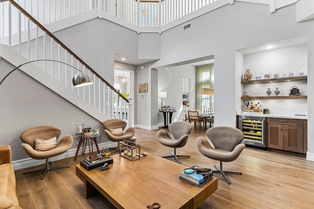 living area featuring beverage cooler, light wood-type flooring, a wealth of natural light, and a bar