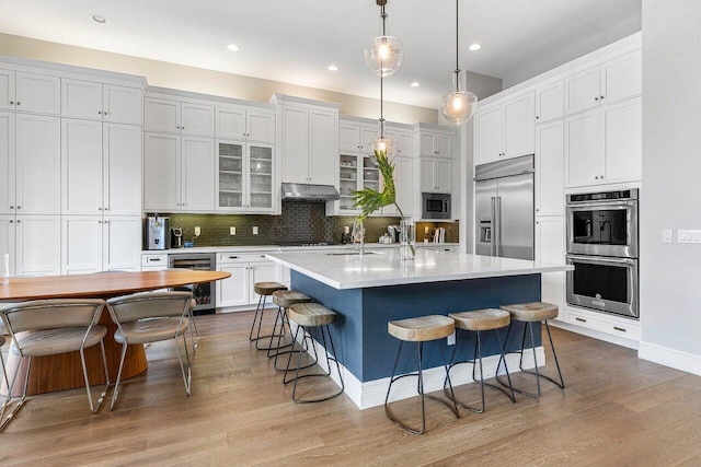 kitchen with light wood-style floors, built in appliances, beverage cooler, a breakfast bar area, and under cabinet range hood