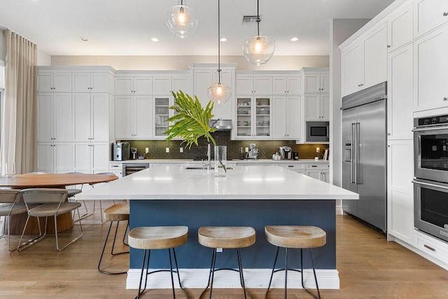 kitchen with built in appliances, white cabinetry, visible vents, and a breakfast bar