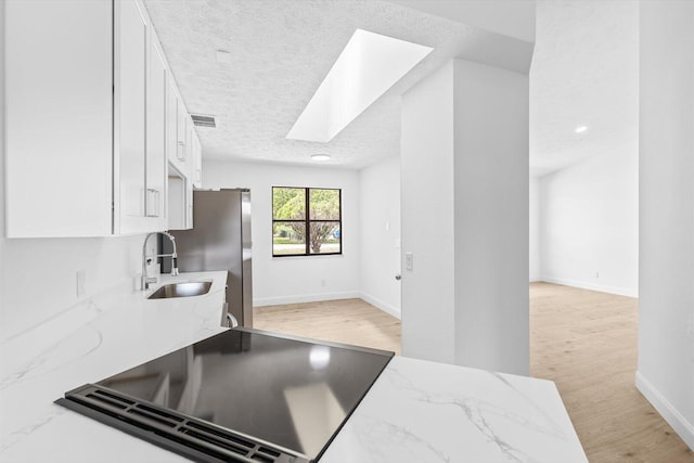 kitchen with light wood finished floors, a sink, white cabinetry, a skylight, and light stone countertops