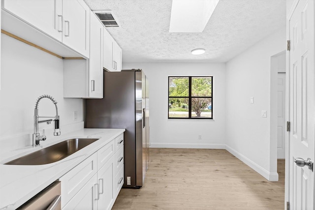 kitchen with light stone counters, a sink, light wood-style flooring, white cabinetry, and visible vents