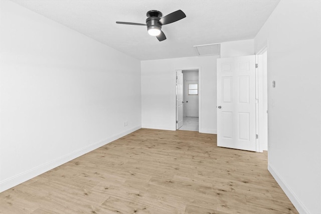 unfurnished bedroom with light wood finished floors, attic access, a ceiling fan, and baseboards
