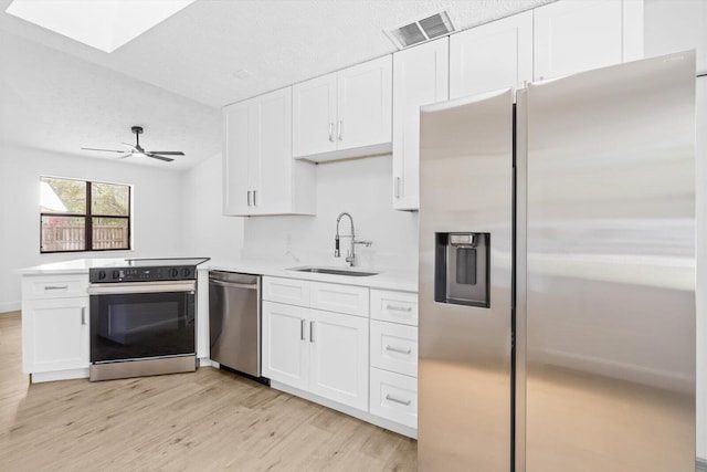 kitchen featuring stainless steel appliances, light wood-style flooring, a sink, visible vents, and white cabinetry