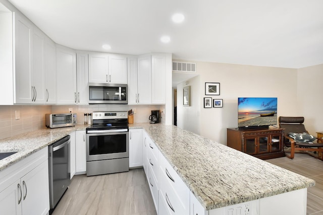 kitchen with stainless steel appliances, a peninsula, a toaster, visible vents, and white cabinetry