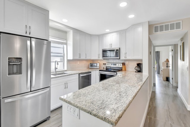 kitchen featuring a sink, decorative backsplash, stainless steel appliances, a peninsula, and visible vents